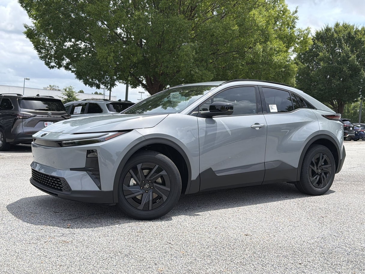 A gray 2026 Toyota C-HR crossover on a dealership lot with trees and other cars behind it.