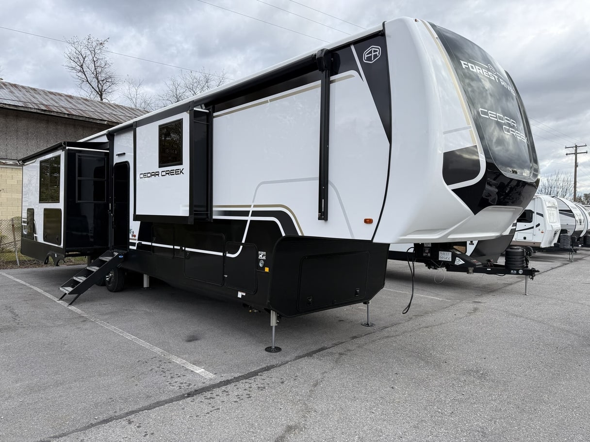 A white Cedar Creek fifth wheel on a paved lot with trees and other trailers behind it.