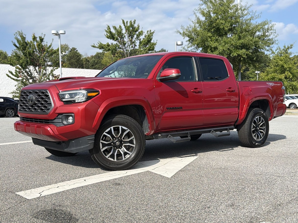 A red 2022 Toyota Tacoma double cab parked on a lot with trees and a light pole behind it.