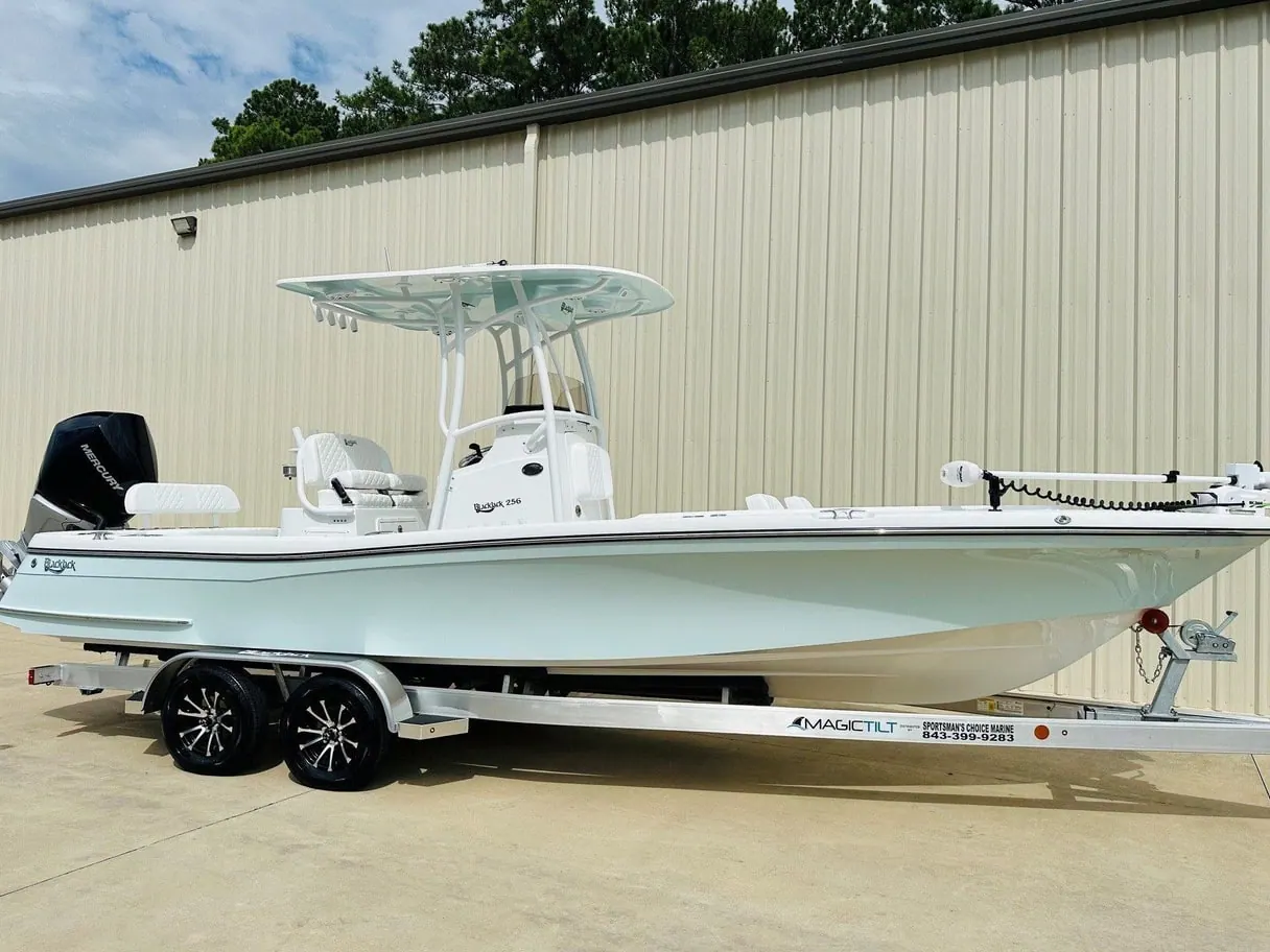A white Blackjack 256 Coastal center console on a trailer in front of a tan metal building.