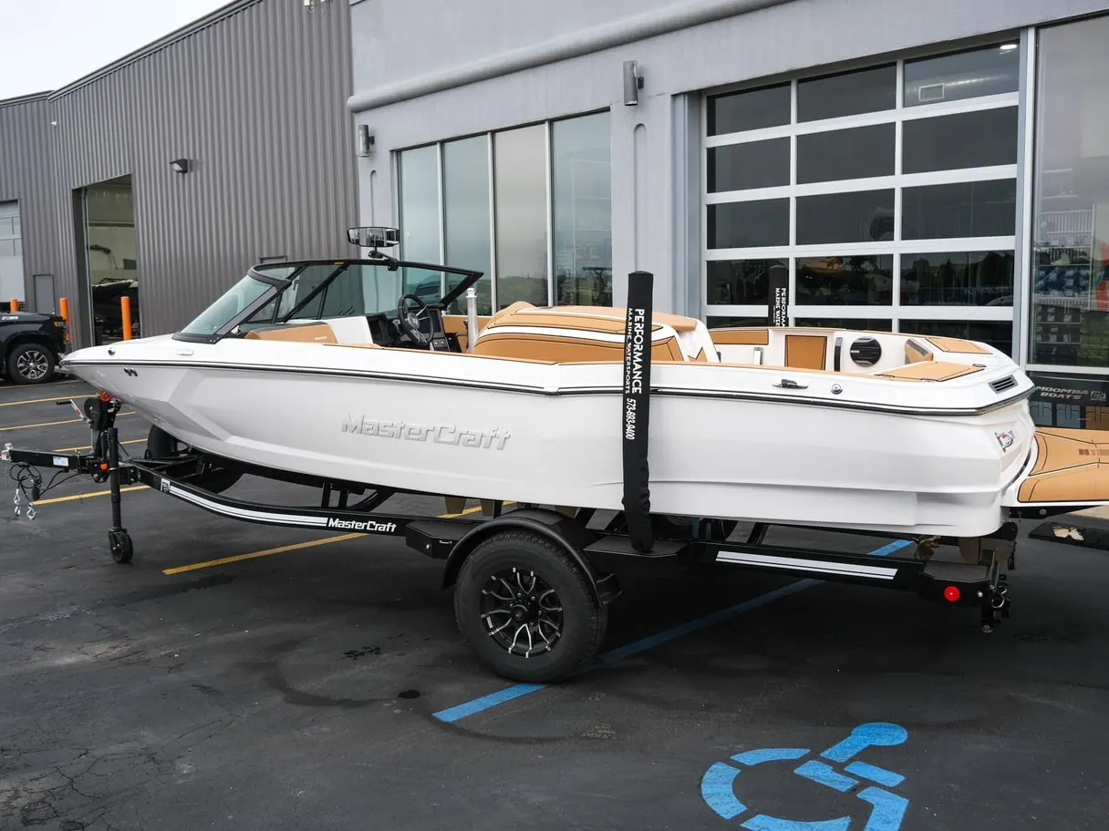 A white MasterCraft ProStar 190 ski boat on a trailer in a parking lot in front of a dealership building.
